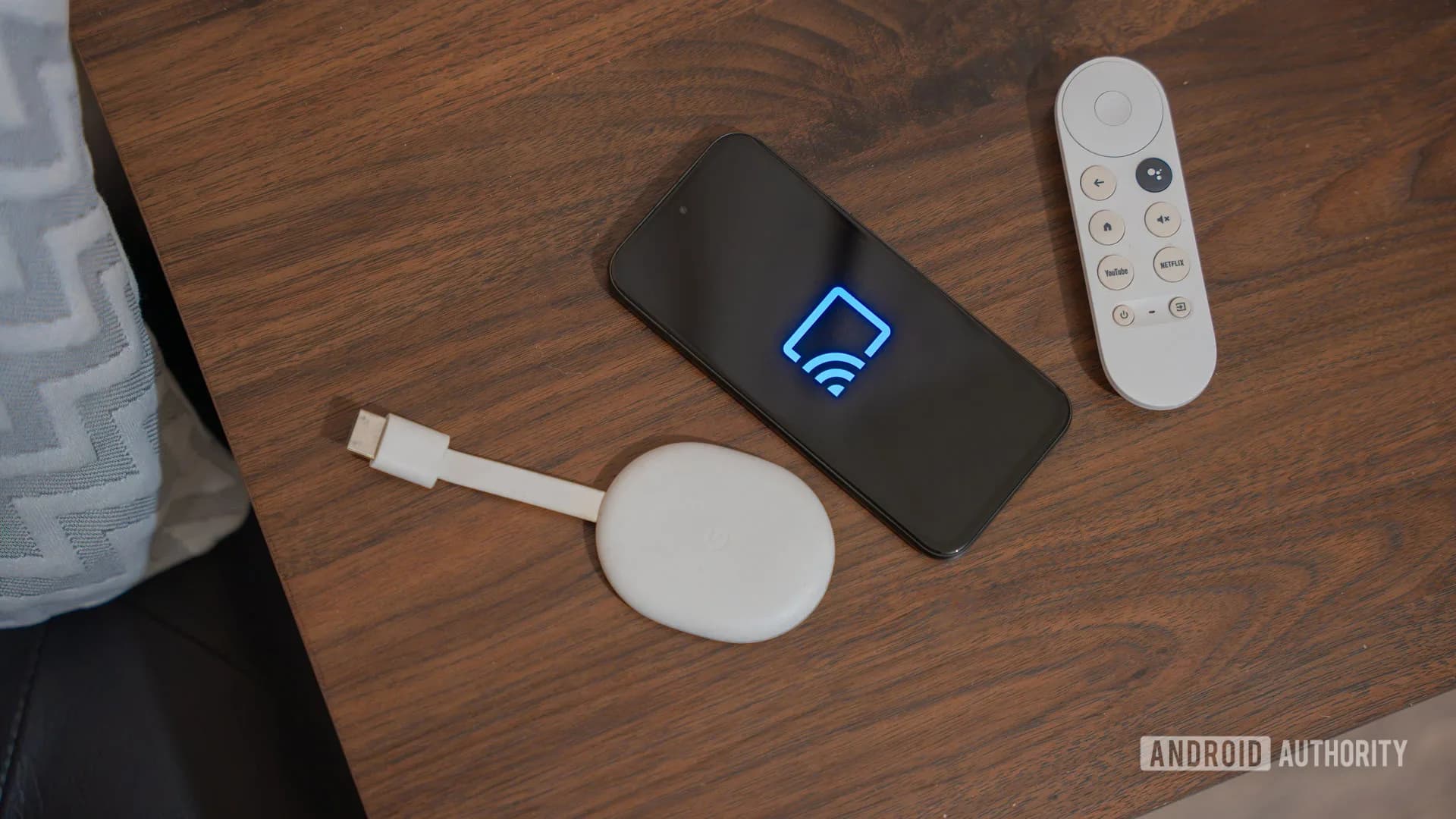 The Chromecast with Google TV dongle and remote control sitting on a surface.