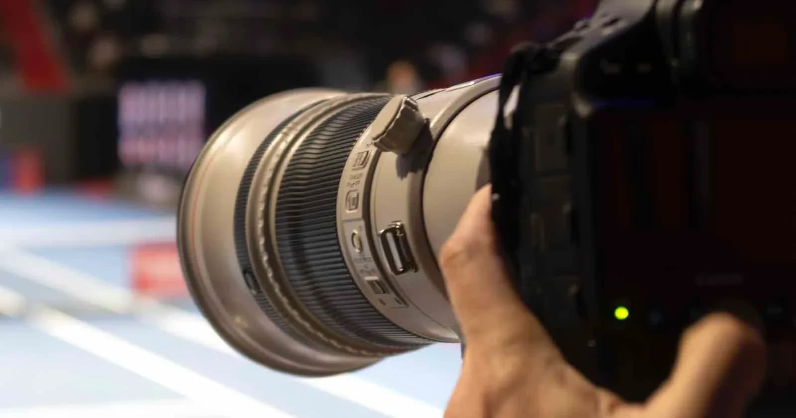 A digital video camera mounted on a tripod overlooking an indoor athletic wrestling arena.