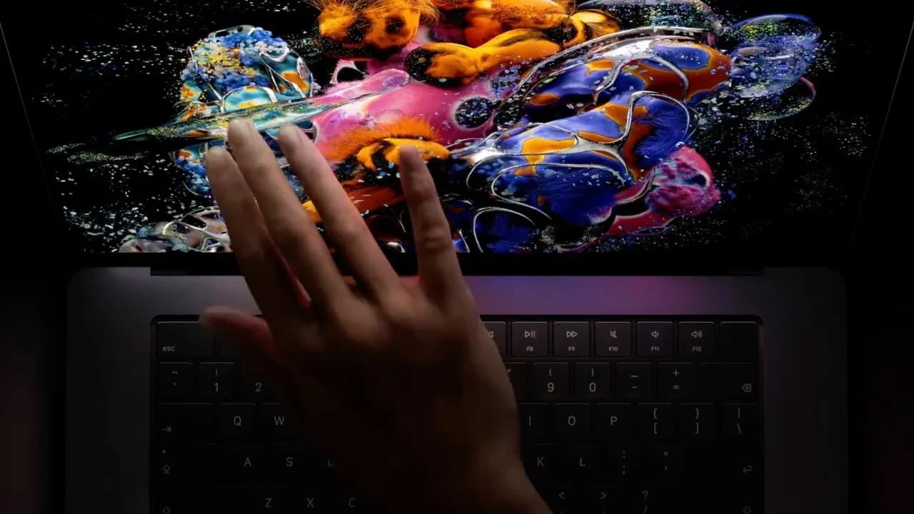 Apple's new MacBook Pro with PROLED XDR touchscreen display open on a desk, showing the Dynamic Island and glowing Apple logo on the lid.