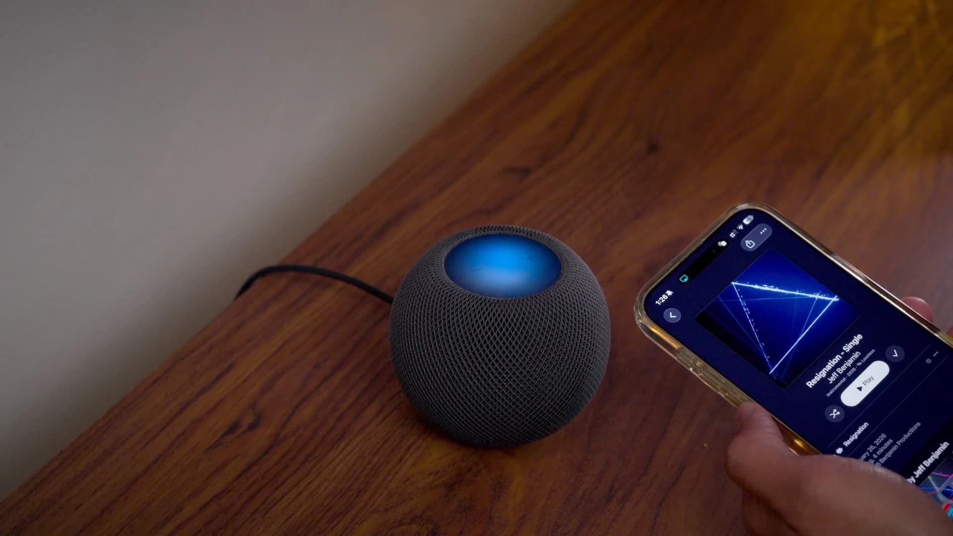 A HomePod with its top cap lit up in colorful animated patterns next to an iPhone showing Home app settings.