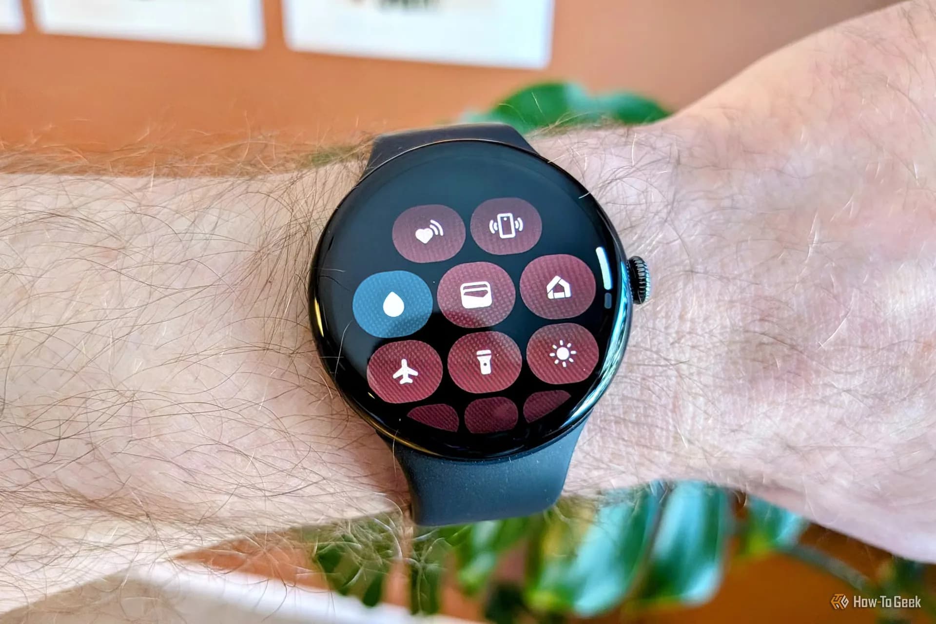 A Pixel Watch on a wrist displaying a Samsung-style watch face and compass interface